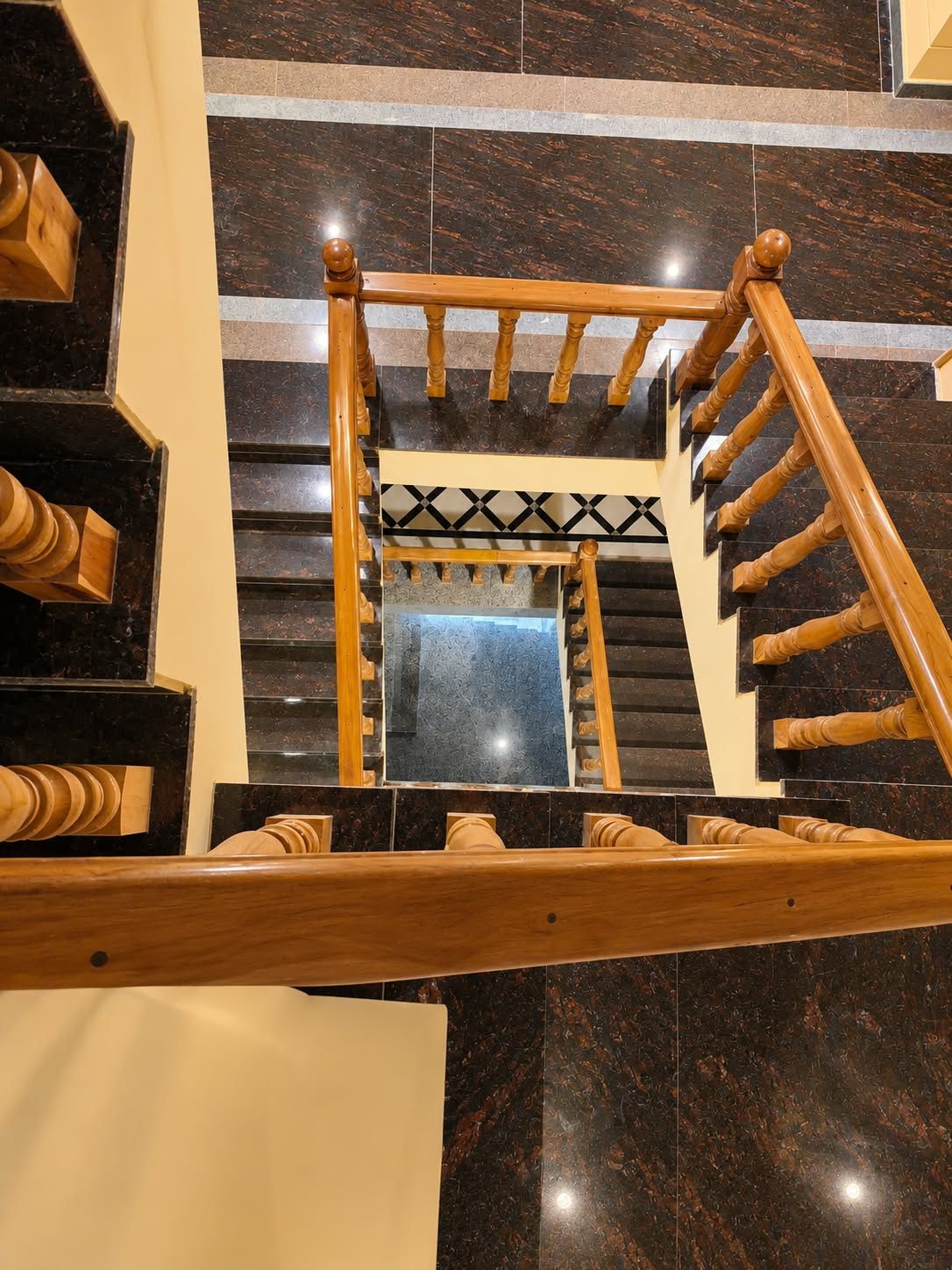 Una escalera de madera con barandilla de diseño geométrico y un espejo que refleja la escalera.