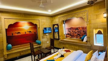 A hotel room with a bed, a television, a wall-mounted TV, and a decorative wall with a desert scene.