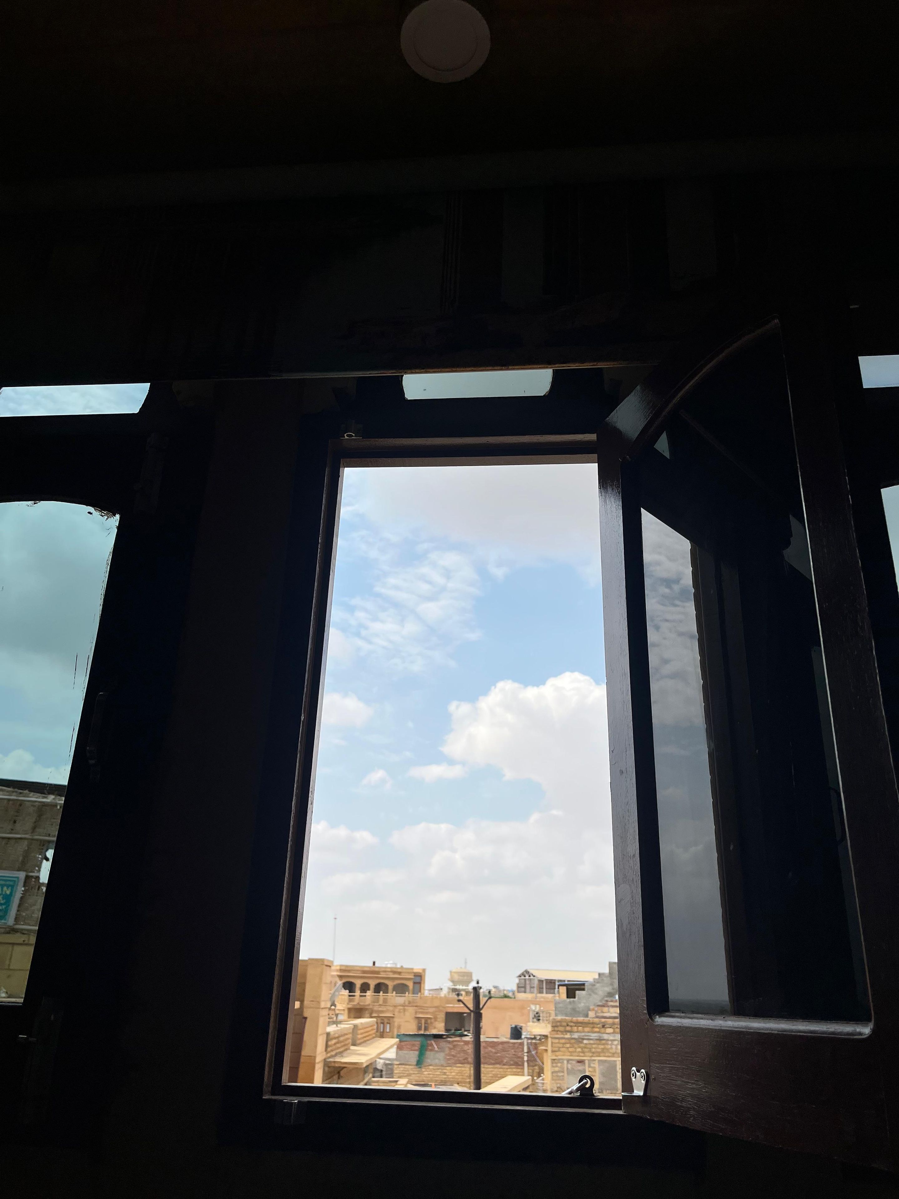 A room with a large window, wooden beams, and a view of buildings outside.