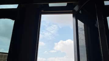 A room with a large window, wooden beams, and a view of buildings outside.