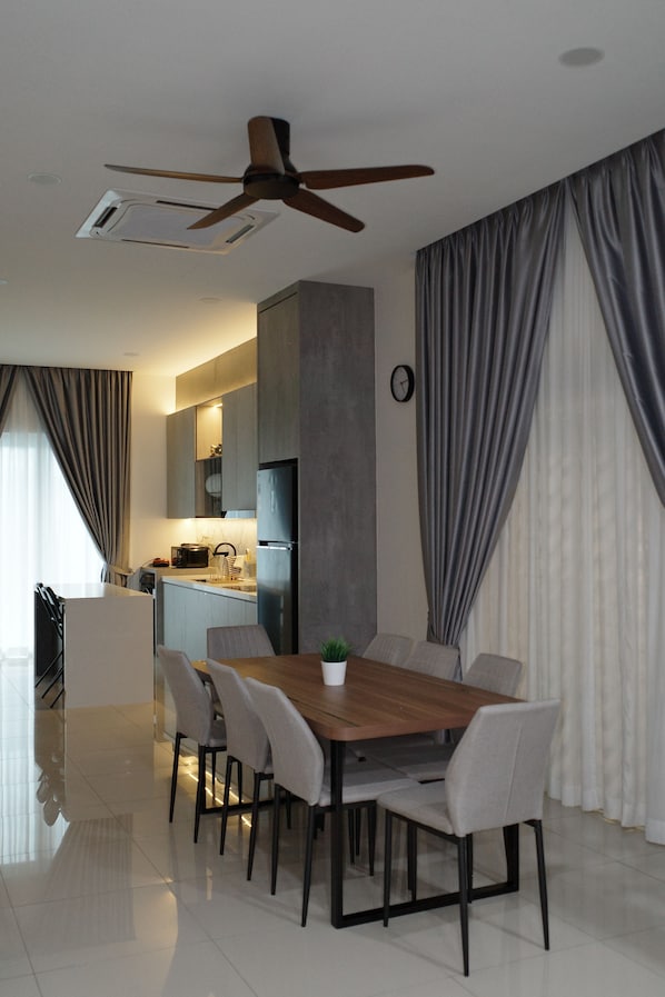A modern dining area with a wooden table and chairs, a ceiling fan, and a view into the kitchen.