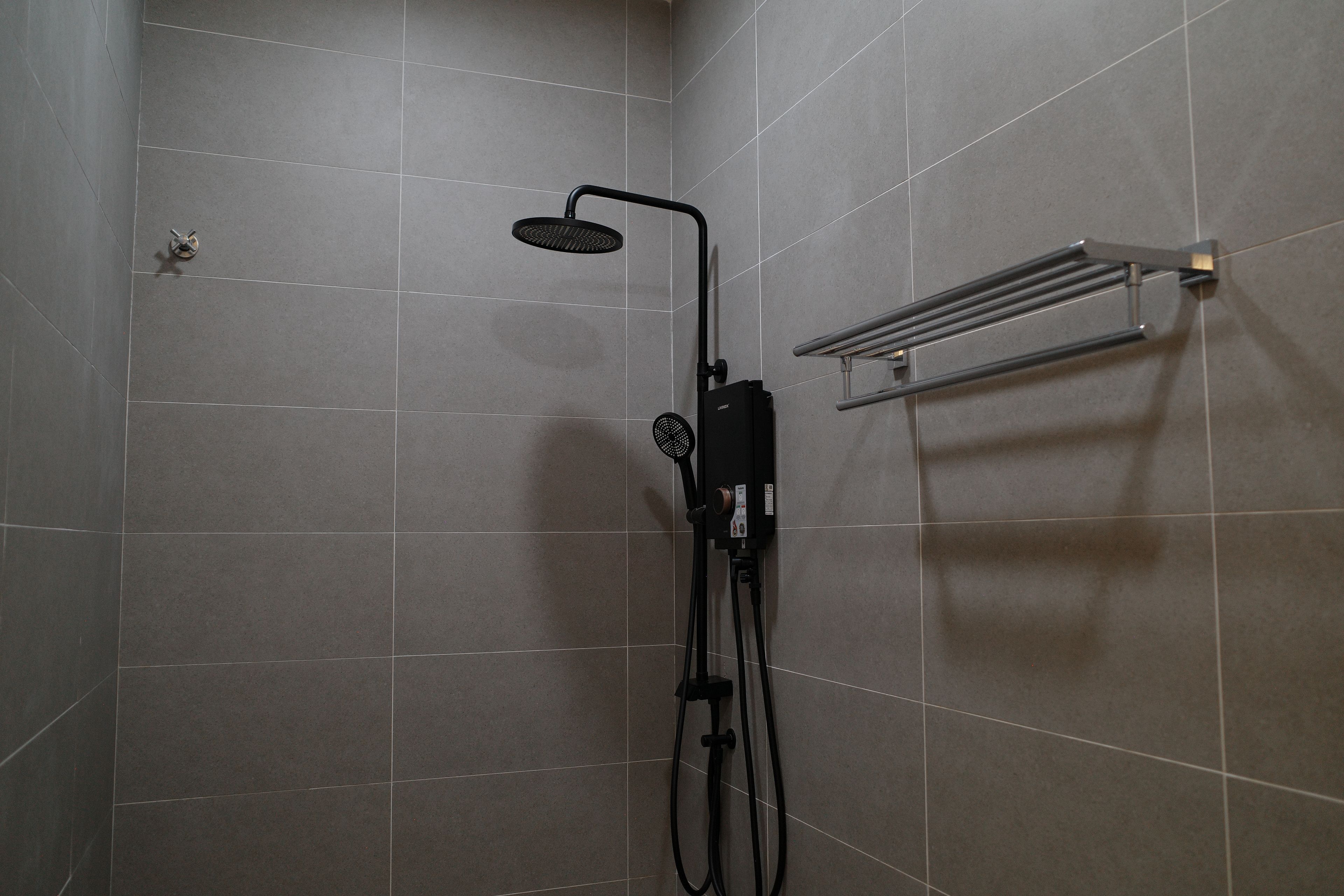 Un espace douche équipé d’un pommeau de douche à main, d’un porte-serviettes mural et d’un panneau de commande.