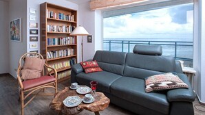 A living room with a sofa, a chair, a bookshelf, and a coffee table. - Holiday apartment with 2 bedrooms (Cuxhaven)