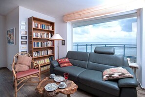 A living room with a sofa, a chair, a bookshelf, and a coffee table. - Holiday apartment with 2 bedrooms (Cuxhaven)