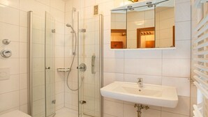 A bathroom with a glass-enclosed shower, a white sink, and a mirror above the sink. - Holiday apartment with 2 bedrooms (Cuxhaven)