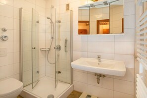 A bathroom with a glass-enclosed shower, a white sink, and a mirror above the sink. - Holiday apartment with 2 bedrooms (Cuxhaven)
