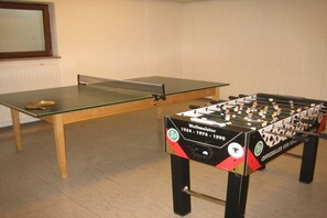 Ein Kicker und ein Tischtennis-Tisch in einem Raum mit hellen Wänden und Holzboden.