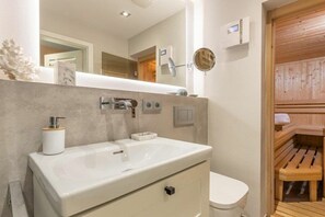 A bathroom with a white sink, a toilet, a mirror, and a wooden sauna door. - Holiday home in Sylt with swimming pool (Sylt)