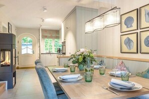 A modern dining area with a wooden table set for four, a fireplace, and framed artwork on the wall. - Holiday home in Sylt with swimming pool (Sylt)