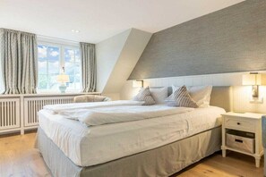 A bedroom with a large bed, two bedside tables, a window with curtains, and a sloped ceiling. - Holiday home in Sylt with swimming pool (Sylt)