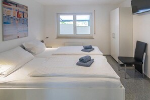 A hotel room with two beds, a window, a flat-screen TV, and a chair. - Holiday apartment with 1 bedroom (Bensersiel)