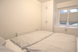 Ein Schlafzimmer mit zwei Betten, einem Fenster mit Jalousien und einer Heizung.