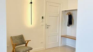 A bathroom with a white door, a chair, a shelf with clothes, and a bathtub.