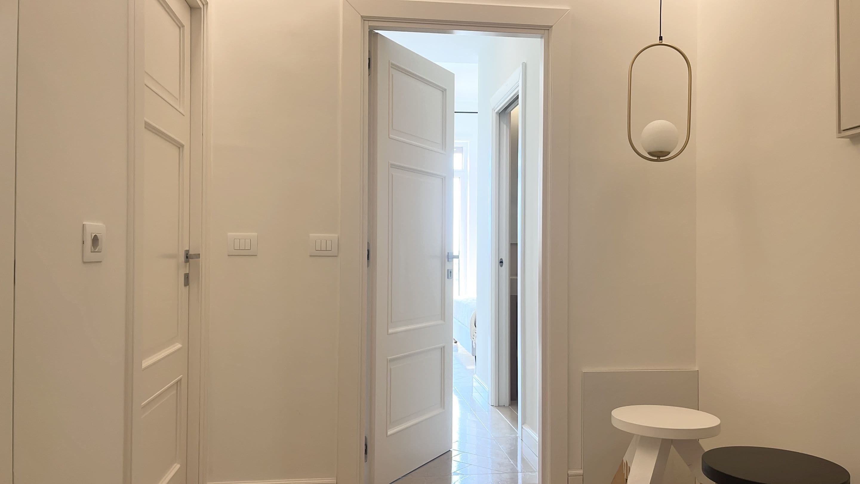 Um corredor com portas brancas, uma pequena mesa redonda e um lustre.