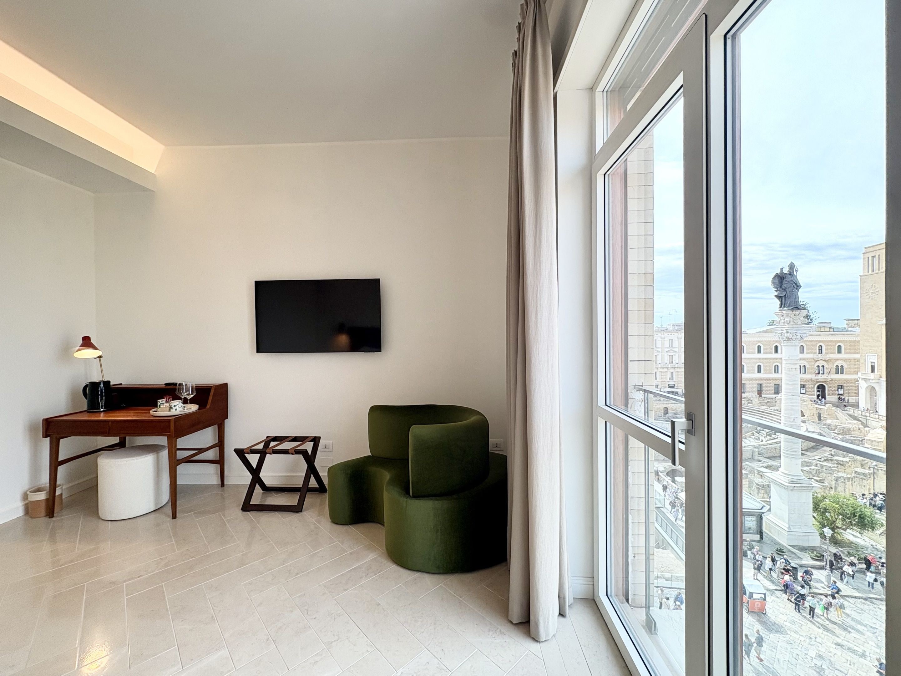Uma sala de estar moderna com televisão de tela plana, uma mesa de madeira, uma poltrona verde e vista para um horizonte urbano através de grandes janelas.