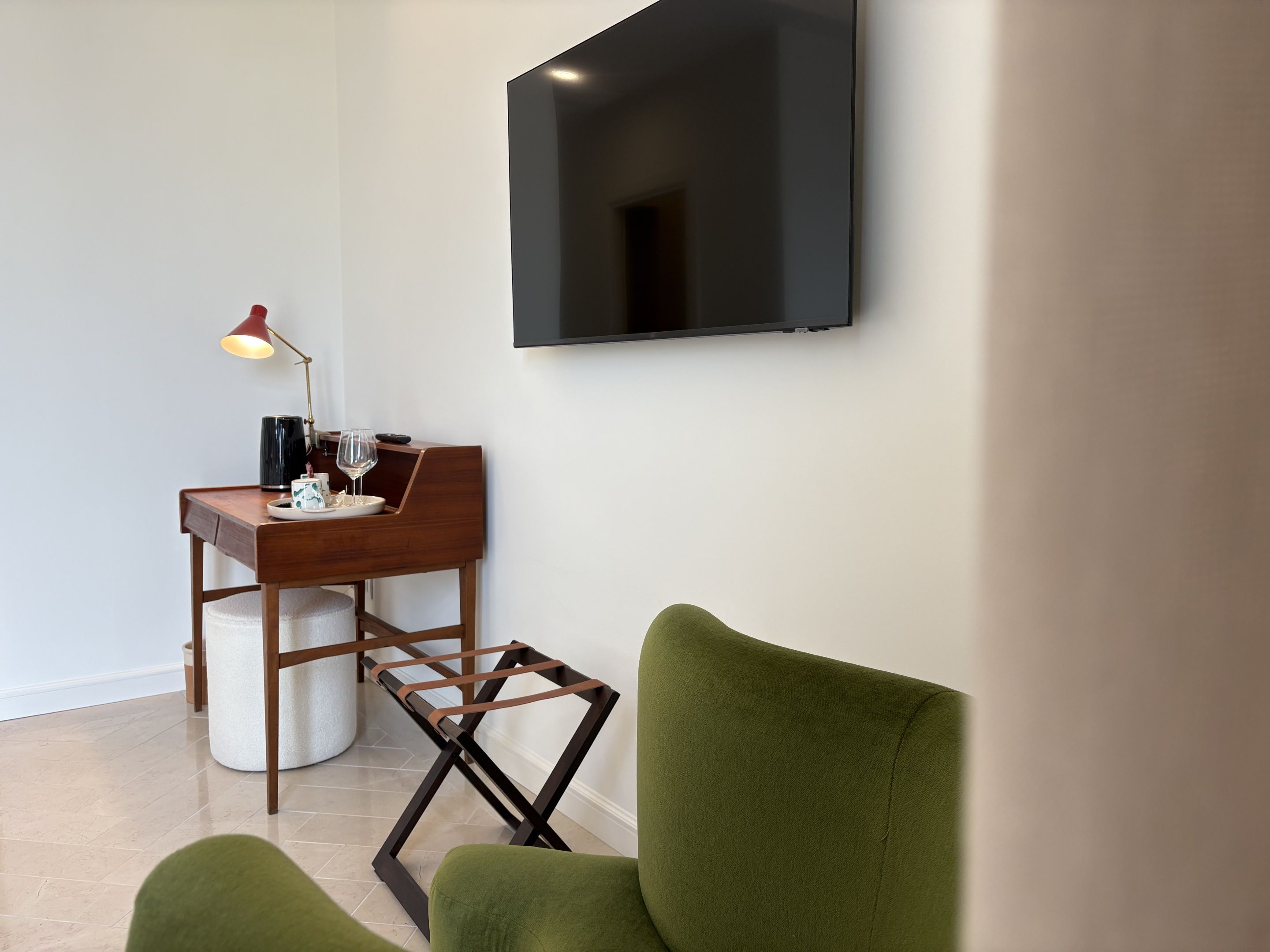 Quarto moderno com televisão de tela plana na parede, escrivaninha de madeira com abajur e poltrona verde.