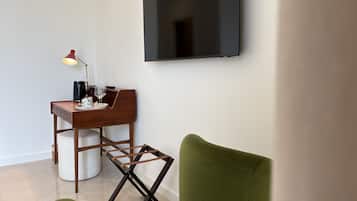 Una camera moderna con una TV a schermo piatto montata a parete, una scrivania in legno con una lampada e una poltrona verde.
