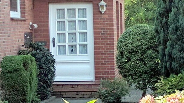 Een bakstenen huis met een witte deur, een klein portaal en een lantaarnpaal.