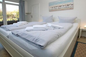 A hotel room with a large bed, a painting on the wall, and a view of the outdoors through the window. - Badestraße 90, Holiday Apartment 1 (Wyk auf Föhr)