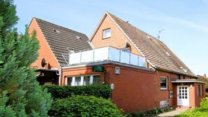 Een gebouw van baksteen met een schuin dak, een klein aanbouwtje met een balkon en een groen bord dat een bedrijf aangeeft.