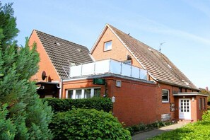 A brick building with a sloped roof, a small attached structure with a balcony, and a green sign indicating a business. - Badestraße 90, Holiday Apartment 1 (Wyk auf Föhr)