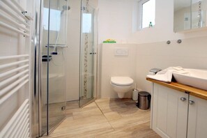 A modern bathroom with a glass-enclosed shower, a toilet, and a sink with a wooden countertop. - Badestraße 90, Holiday Apartment 1 (Wyk auf Föhr)