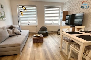 Ein modernes Wohnzimmer mit einer Couch, einem Esstisch, einem Fernseher und einer dekorativen Lampe.