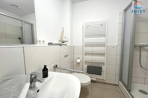 Ein modernes Badezimmer mit Waschbecken, Toilette und Duschbereich in Weiß.