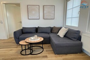 A modern living room with a grey sectional sofa, a small round wooden coffee table, and two abstract wall art pieces. - 333 - Holiday Apartment 3 (Juist)