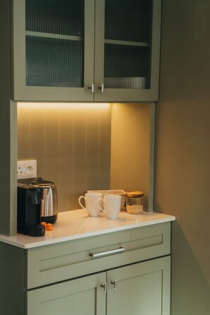 Eine Küchenzeile mit Kaffeemaschine, Tassen und einem Glas auf der Arbeitsfläche.