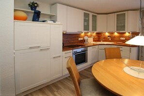 A modern kitchen with white cabinetry, a wooden countertop, and a dining area with a round table and wicker chairs. - Kiek Ut 9, Holiday Apartment 2 (Wyk auf Föhr)