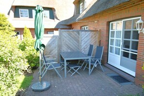 An outdoor patio with a table and chairs, a green umbrella, and a brick wall. - Kiek Ut 9, Holiday Apartment 2 (Wyk auf Föhr)