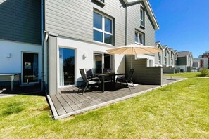 Ein modernes, zweistöckiges Haus mit einer Terrassenfläche, komplett mit Tisch, Stühlen und einem großen Sonnenschirm.