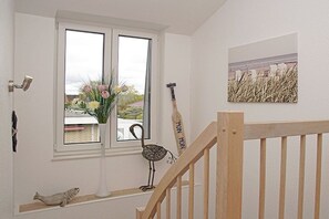 A staircase with a wooden handrail and a white wall with a window, a vase with flowers, and a small sculpture. - Holiday home in Duhnen with Wi-Fi and parking (Duhnen)