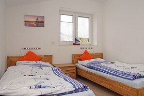 Ett sovrum med två separata sängar, var och en med en sänggavel i trä, ett nattduksbord och ett fönster med persienner.