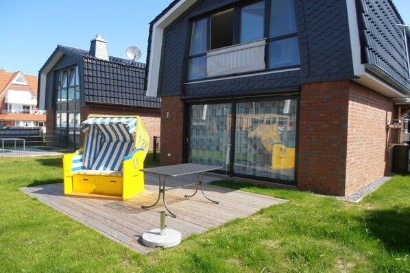 A modern house with a large glass window, a yellow chair, and a table on a wooden deck. - Holiday home in Duhnen with Wi-Fi and parking (Duhnen)