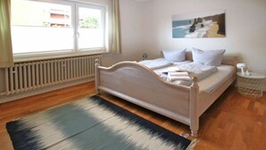 Een slaapkamer met een bed, een raam, een radiator en een schilderij aan de muur.