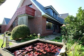 A house with a brick exterior, a red balcony, a small pond with lily pads, and a well. - Linge 4, Holiday Apartment 1, Hygge (Wrixum)