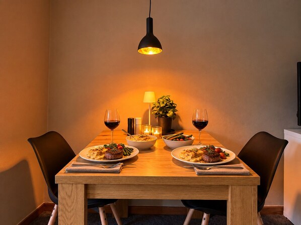 Una mesa de comedor con dos platos de comida, dos copas de vino, una lámpara, velas y una planta en maceta.