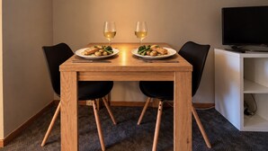 Uma sala de jantar com mesa de madeira, duas cadeiras, dois pratos de comida e dois copos de vinho branco.