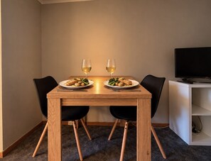 En matplats med ett träbord, två stolar, två tallrikar med mat och två glas vitt vin.