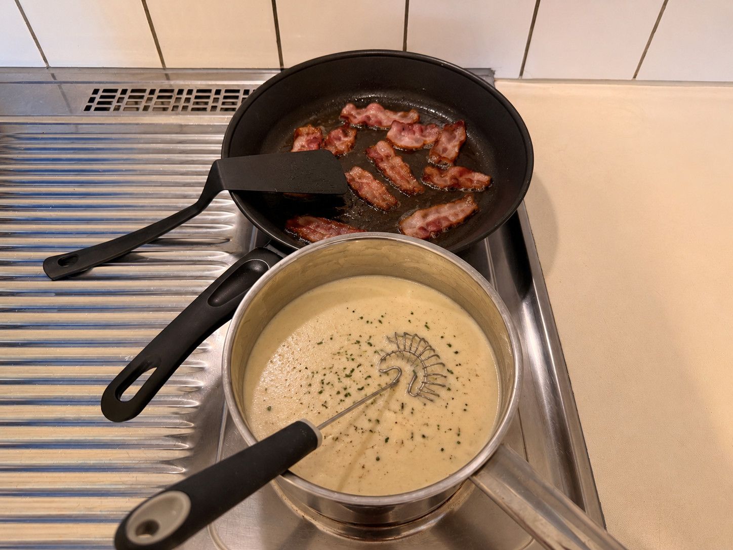 A kitchen with a frying pan on the stove and a pot with a whisk in it.