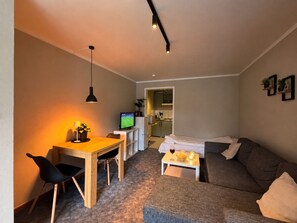 A compact living space with a dining area, a television, a sofa, and a small kitchen area.