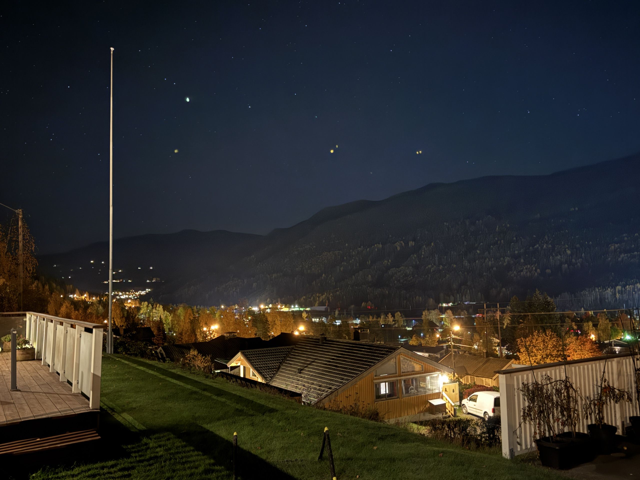 Un quartier résidentiel avec des maisons, un mât de drapeau et un ciel nocturne dégagé.