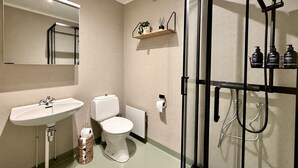Casa de banho com lavatório, sanita e zona de duche com cabine de vidro.