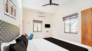 A hotel room with a bed, a desk with a chair, a ceiling fan, and a window with blinds.