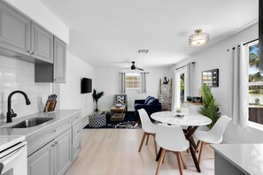 A modern kitchen with white cabinetry, a black faucet, and a dining area with a round table and white chairs. - Lake Patio + Firepit + Grill | Mins to Vanderbilt Beach | Fisherman's Cottage (Naples)