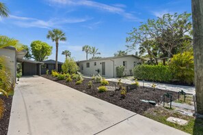 A residential area with a paved driveway leading to a row of houses, surrounded by landscaped gardens and palm trees. - Lake Patio + Firepit + Grill | Mins to Vanderbilt Beach | Fisherman's Cottage (Naples)