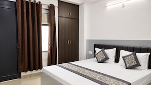 Un dormitorio con cama, cortinas, armario y mesita de noche.