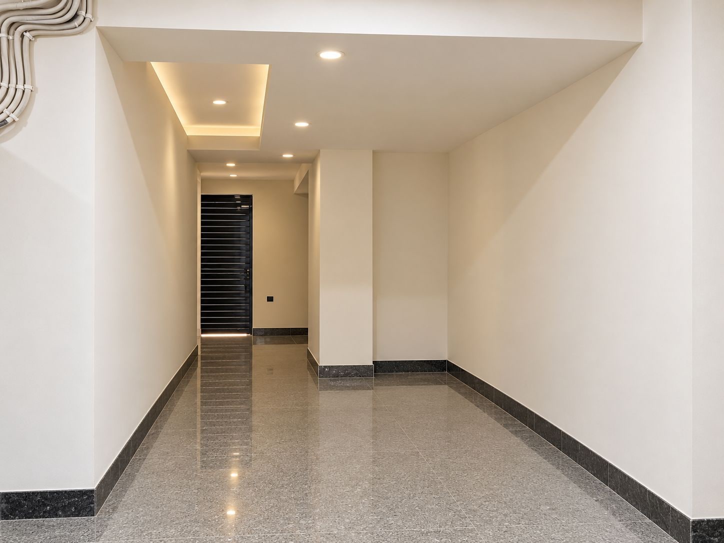 A modern hallway with a polished floor, recessed lighting, and a door at the end.